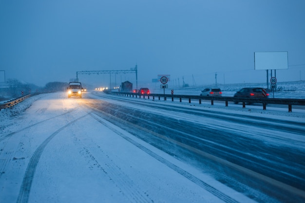 Samochody jeżdżą po autostradzie wieczorem podczas śnieżycy.