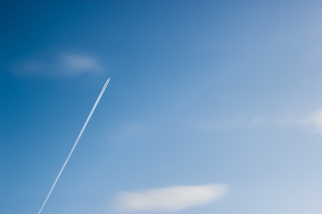 Samolot leci ukośnie po błękitnym niebie wśród chmur i słońca