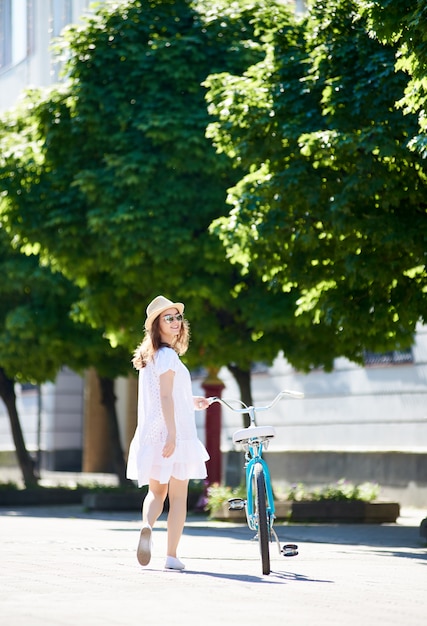 Samotna dziewczyna jest wyposażona w retro rower na słonecznej ulicy miasta z zielonymi terenami