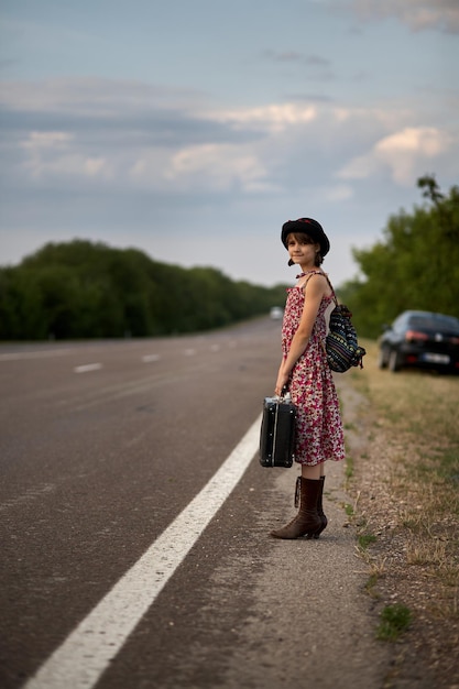 Samotna dziewczyna z walizką stojąca na drodze