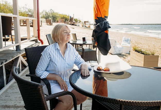Zdjęcie samotna kobieta siedzi przy stoliku w kawiarni nad morzem i patrzy na fale. w tle widać ludzi