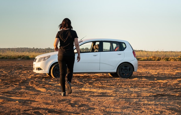 Samotna kobieta w ciemnych ubraniach zbliża się do białego samochodu o wschodzie słońca