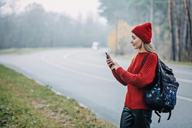 Samotna kobieta z plecakiem w pobliżu drogi na tle lasu hipsterska dziewczyna wanderlust chodząca po asfalcie