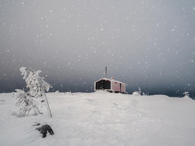 Samotny czerwony pensjonat na ośnieżonym stoku zimą pod dramatycznym nocnym niebem Zimowe schronienie dla turystów Dom na górze