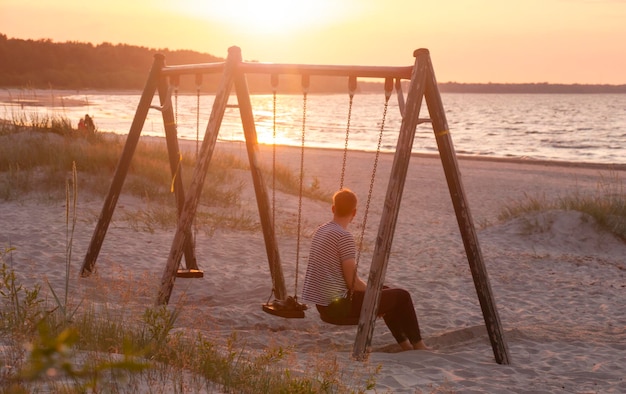 Samotny mężczyzna na huśtawce podziwia zachód słońca na morskiej piaszczystej plaży