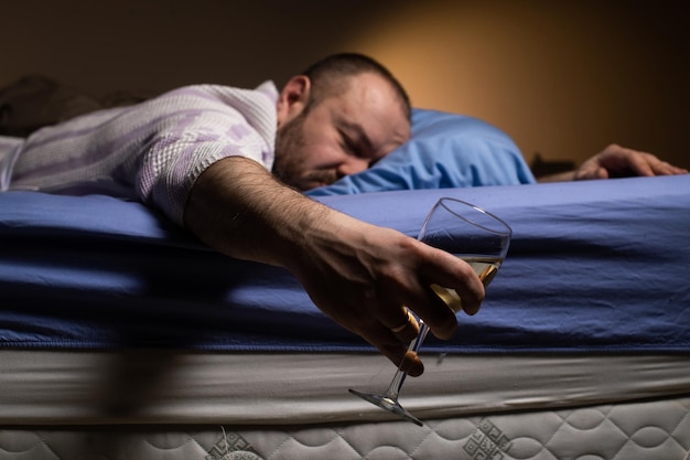 Zdjęcie samotny mężczyzna z kieliszkiem wina w łóżku alkoholizm samotność pij alkohol na sen ciemny pokój