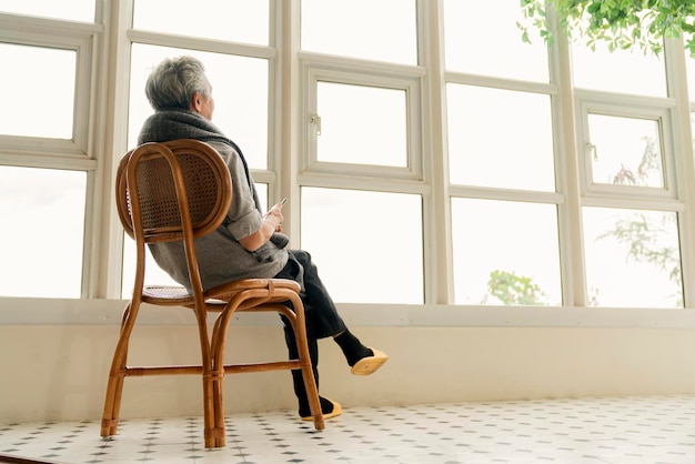 Samotny starszy mężczyzna w podeszłym wieku mężczyzna cieszący się patrzeniem przez okno w domu widok z oknaWidok z boku starszego mężczyzny cierpiącego na przewlekłą chorobę Alzheimera siedzącego w salonie