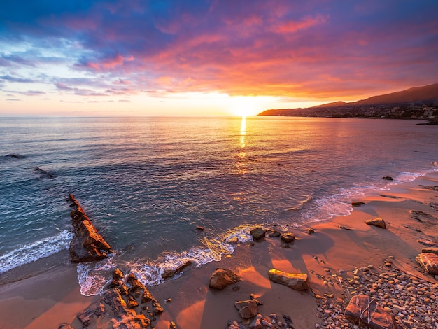 Sanremo Riviera dei Fiori Liguria Włochy Scenis skały i kamyki na plaży oświetlone pięknym światłem zachodu słońca Dramatyczne kolorowe niebo falujące morze