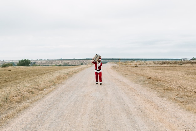Santa Claus niosąc walizkę podróżną w wiejskim krajobrazie. Podróżuj na Boże Narodzenie koncepcji