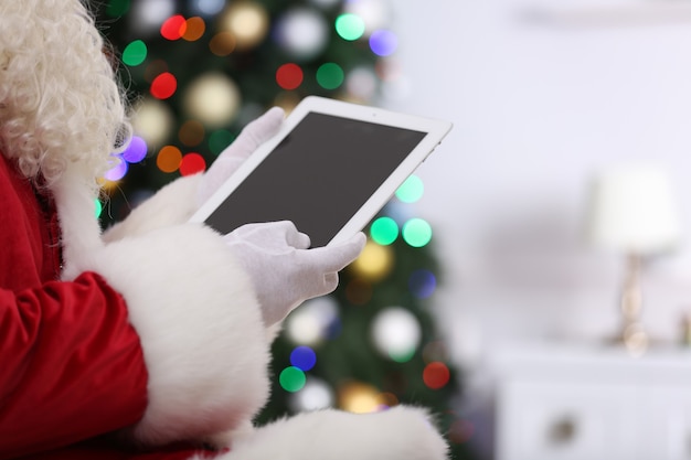 Santa trzymając tablet na tle choinki