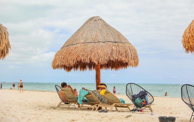 Scena na plaży z leżakiem i parasolem krytym strzechą.