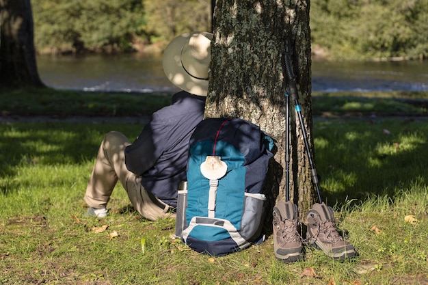 Scena Plecaka Opartego O Drzewo, Buty I Akcesoria Oraz Pielgrzyma Odpoczywającego W Drodze Do Santiago De Compostela. Koncepcja Camino De Santiago