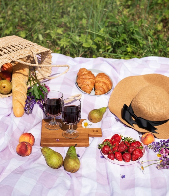 Scena romantycznego pikniku w letni dzień. Piknik na świeżym powietrzu z winem i owocami na świeżym powietrzu na tle zielonej trawy.