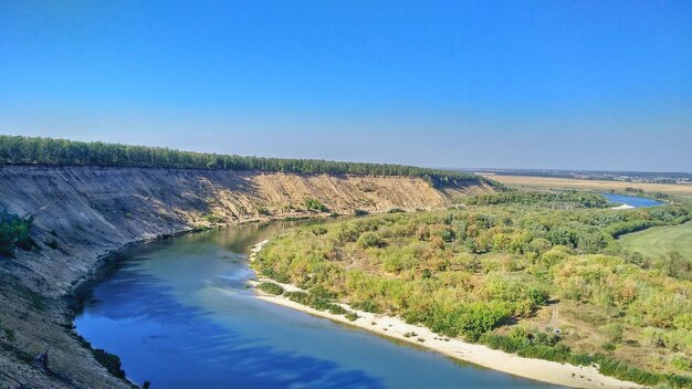 Zdjęcie sceniczny widok rzeki pośród krajobrazu na tle jasnego niebieskiego nieba