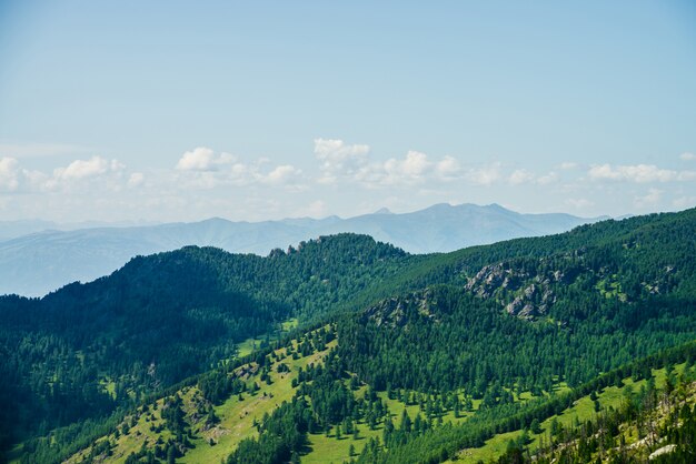 Sceniczny widok z lotu ptaka zielonego lasu wzgórza i długi pasmo górskie pod niebieskim niebem. Niesamowity, minimalistyczny alpejski krajobraz rozległych połaci. Cudowna żywa góralska sceneria z pięknymi górami i lasem.