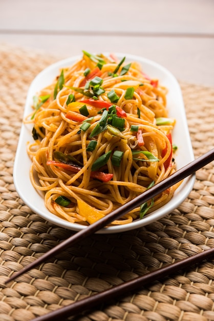 Schezwan Noodles lub warzywny makaron Hakka lub chow mein to popularne przepisy indochińskie, podawane w misce lub talerzu z drewnianymi pałeczkami. selektywne skupienie