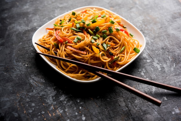 Schezwan Noodles lub warzywny makaron Hakka lub chow mein to popularne przepisy indochińskie, podawane w misce lub talerzu z drewnianymi pałeczkami. selektywne skupienie