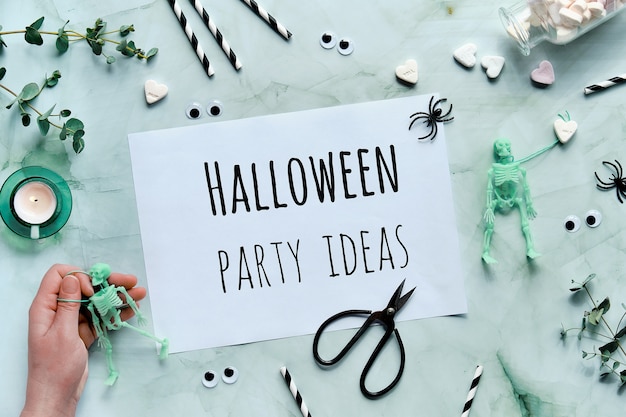 Schowek z tekstem Pomysły Halloween Party na miętowym tle. Leżał płasko ze szkieletem w dłoni,