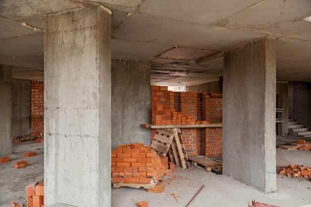 Ściany wielopiętrowego domu z czerwonej cegły. Plac budowy, narzędzia, taczka, piasek i cegły przy budowie nowego domu, betoniarka i akcesoria