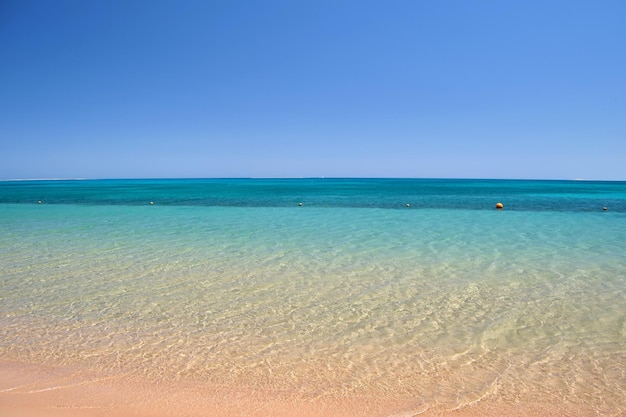 Seascape z powierzchnią błękitnej wody morskiej z małymi falami rozbijającymi się o żółtą piaszczystą plażę. Koncepcja podróży i wakacji.