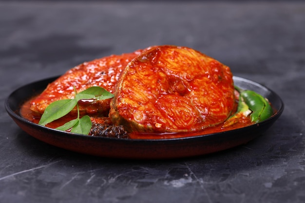 Seer Fish curry Indyjskie curry rybne ułożone w czarnej misce przyozdobionej tamaryndą malabarską