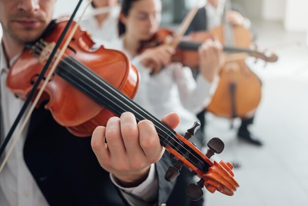 Sekcja smyczkowa orkiestry symfonicznej muzyki klasycznej wykonująca męskiego skrzypka grającego na pierwszym planie muzyki i koncepcji pracy zespołowej