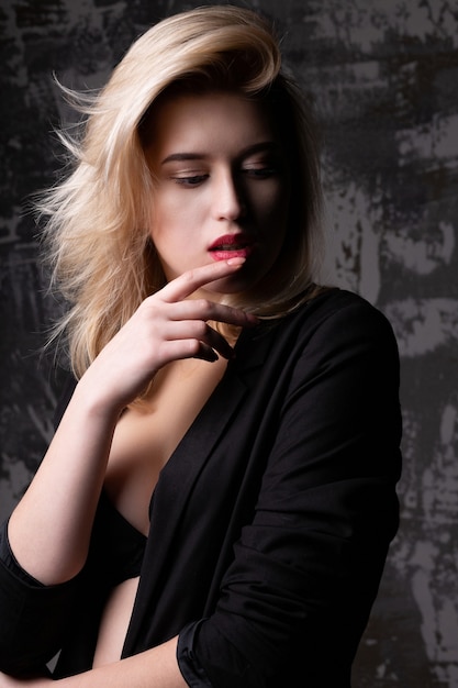 Seksowna blond modelka z idealną skórą, ubrana w czarną kurtkę i biustonosz, pozowanie w studio z cieniami