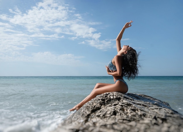 Seksowna dziewczyna w stroju kąpielowym pozuje szczupły na białej skale na tle morza