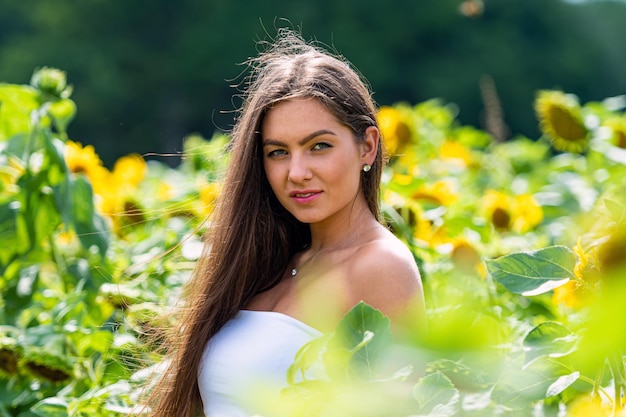 Seksowna młoda brunetka z długimi włosami w polu słoneczników na letni dzień kobieta otoczona słonecznikami