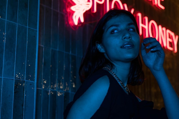 Seksowna młoda piękna kobieta pozuje nad nocnym miastem dramatycznym czerwonym i niebieskim neonowym tle
