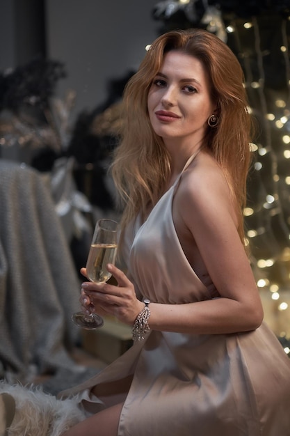 Seksowna modelka w średnim wieku z kieliszkiem szampana na imprezie pije szampana na wakacyjnym świecącym niebieskim tle Pewna siebie nowoczesna dama na nocnej imprezie