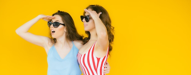 Seksowne beztroskie kobiety pozują przy żółtej ścianie w okularach przeciwsłonecznych Pozytywne modele idą