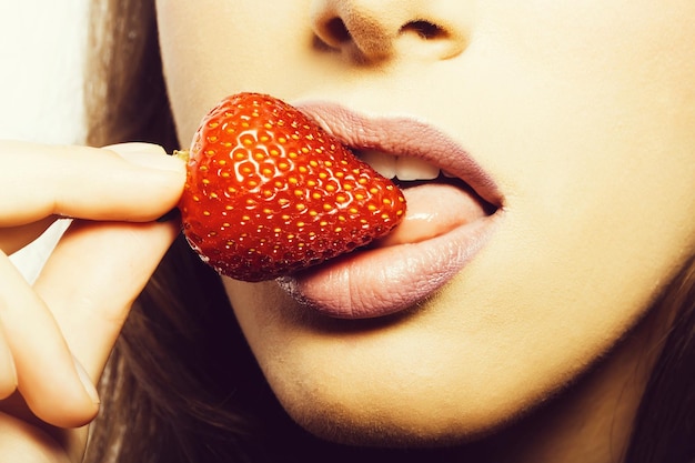 Zdjęcie seksowne kobiece usta z różową szminką na ustach, jedzenie i lizanie językiem czerwony słodki truskawkowy owoc jagodowy trzymając w ręku zbliżenie