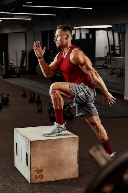Seksowni muskularni mężczyźni korzystający z platformy do nóg na ciemnym kolorowym tle siłowni.