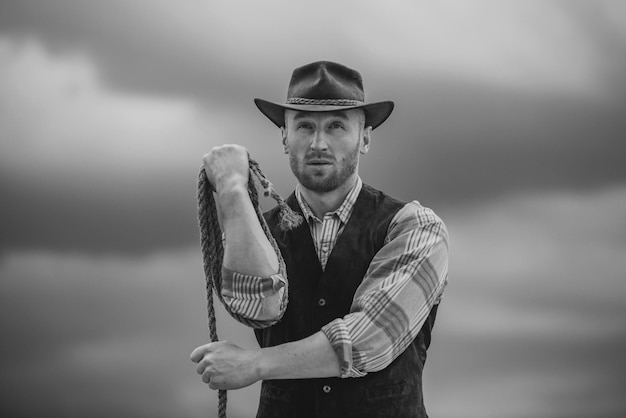 Seksowny mężczyzna z westernu w kowbojskim kapeluszu Kowboj z liną lasso na tle nieba