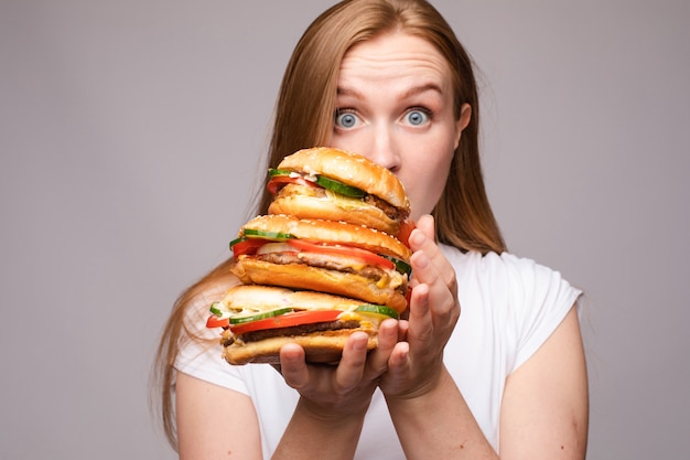 Selekcyjna ostrość dużych smacznych hamburgerów w rękach zdumionej dziewczyny