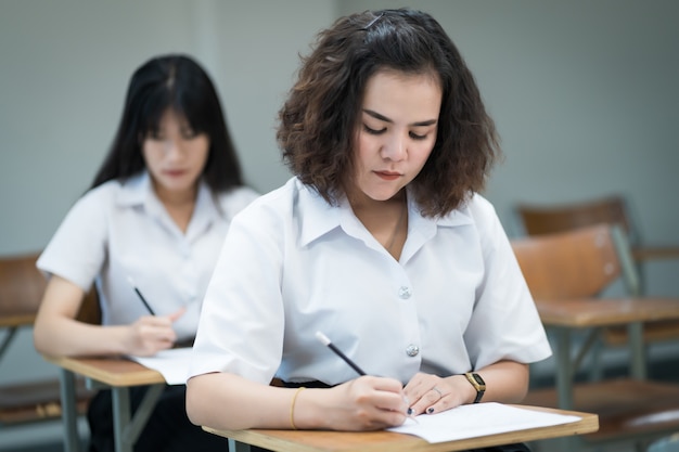 Selektywna Koncentracja Nastoletnich Studentów Siedzących Na Krześle Wykładowym W Klasie Napisz Na Arkuszu Odpowiedzi Egzaminacyjnej Podczas Wykonywania Końcowego Testu Egzaminacyjnego. Uczennice W Mundurkach Studenckich.