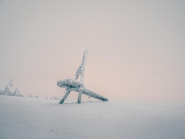 Selektywne skupienie. Minimalistyczne zimowe tło z zamarzniętym drewnianym krzesłem z mroźną mgiełką na tle różowego nieba polarnego dnia.