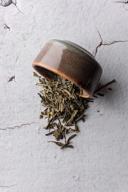 Selektywne skupienie naturalnej zielonej herbaty liściastej do parzenia w glinianej misce z pionowym kątem makro na jasnym tle...
