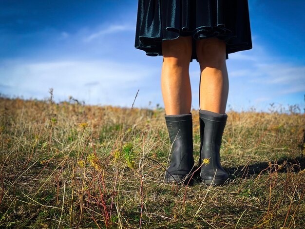 Zdjęcie selektywne skupienie się na kobiecie w czarnych butach i niebieskiej sukience stojącej na środku pola