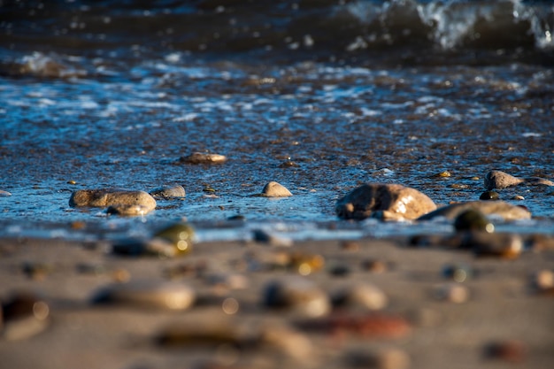 Selektywne skupienie się na piasku i kamieniach plaży z łamaczem morskim w tle