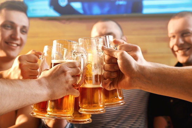 Selektywne skupienie się na szklanki piwa w rękach wesołych przyjaciół płci męskiej w pubie