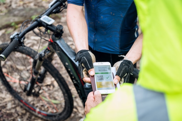 Selektywne Skupienie, Sportowiec Na Rowerze Górskim Pokazuje Paszport Zdrowia Z Certyfikatem Szczepień Przez Telefon Na Torze Wyścigowym, Aby Potwierdzić, że Został Zaszczepiony Przeciwko Koronawirusowi. Sport Podczas Pandemii Covid-19.