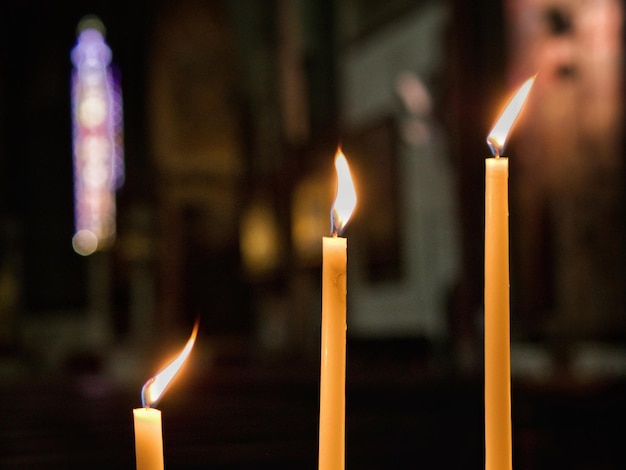 Selektywne skupienie trzech zapalonych świec w kościele na ciemnym, niewyraźnym tle