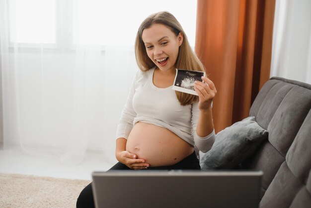 Selektywne skupienie wesołej kobiety w ciąży pokazującej zdjęcia USG podczas rozmowy wideo