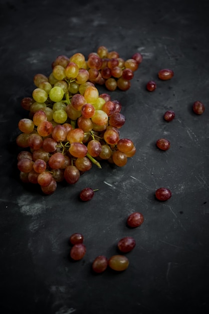 Selektywne ustawianie ostrości, soczyste czerwono-zielone winogrona na ciemnym stole w niskim tonie, martwa natura