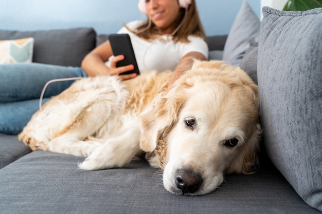 Selektywny Fokus Kaukaski Kobieta Słuchania Muzyki W Swoim Telefonie Z Psem. Poziomy Widok Przygnębionego Psa Leżącego Na Kanapie. Styl życia Ludzi I Psów.