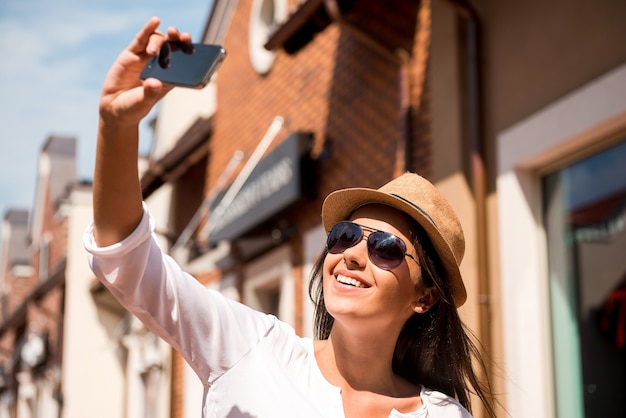 Selfie! Piękna młoda funky kobieta robi selfie stojąc na zewnątrz