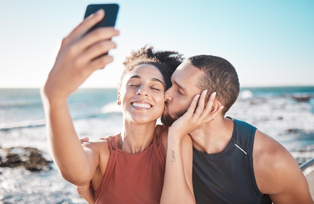 Selfie pocałunek wdzięczności i para z telefonem do przesyłania strumieniowego treningu i miłości na plaży na Bali Troskliwe ćwiczenia i czuły mężczyzna i kobieta z uśmiechem na mobilne zdjęcie po treningu