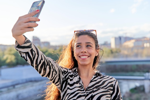 Selfie szczęśliwej i wesołej Latynoski w swobodnym ubraniu Podekscytowana Latynoska dziewczyna uśmiecha się i robi zdjęcie ze smartfonem